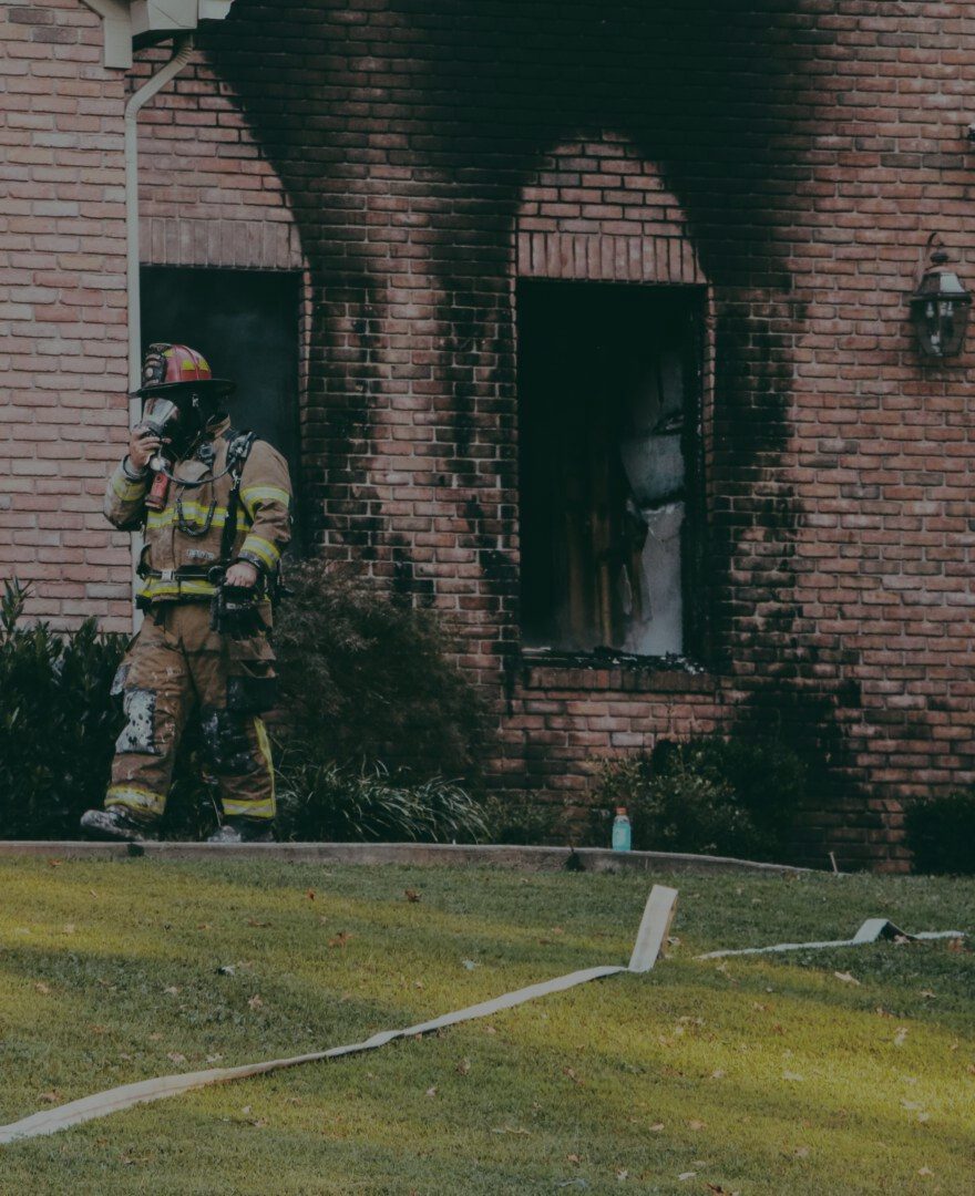 Firefighter walking past a fire-damaged brick home